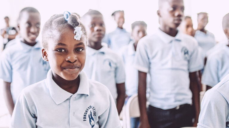 Bambina corista di ABF Voices of Haiti che sorride durante le prove con gli altri coristi sullo sfondo